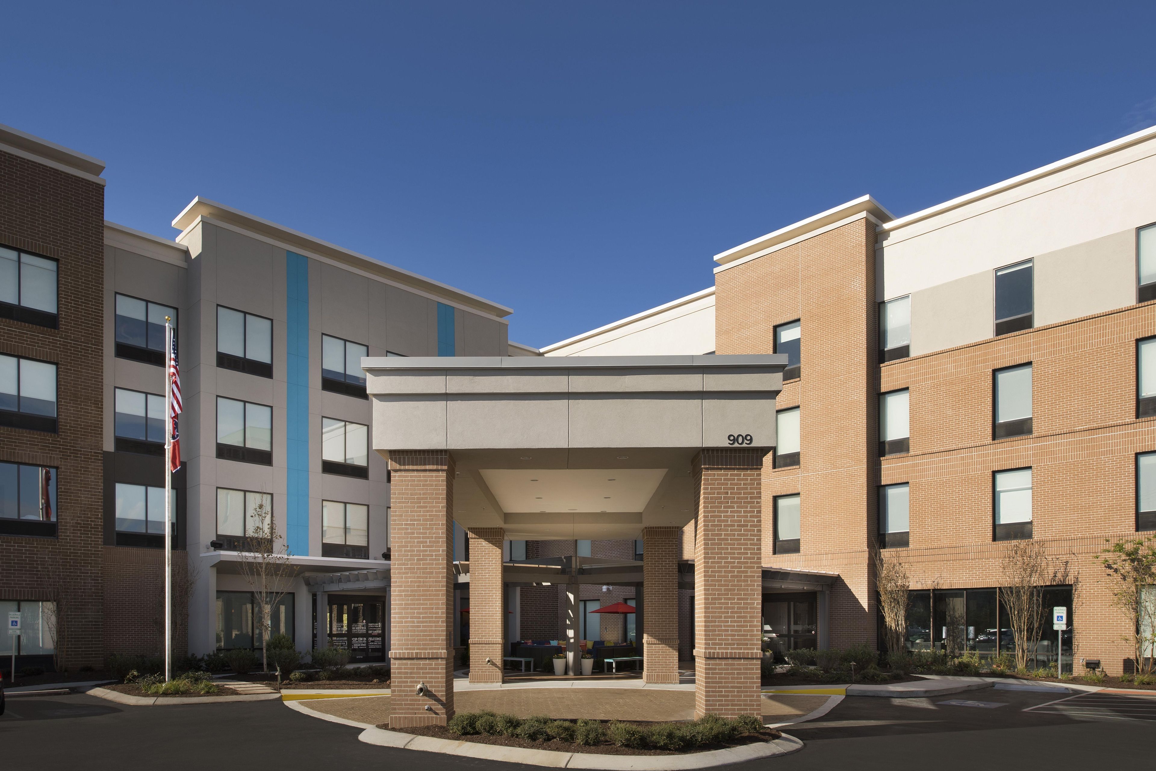 A modern building with a covered entrance, multiple windows, and a brick facade.