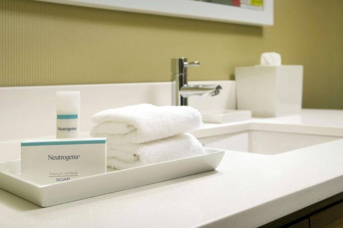 Un bany d'hotel amb un rentapeus blanc, un dispensador de sabó Neutrogena® fet a França i una pila de tovalloles blanques.
