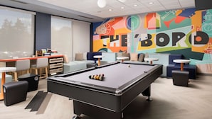 A pool table in a modern lounge area with a colorful mural and comfortable seating. - Home2 Suites by Hilton Murfreesboro (Murfreesboro)