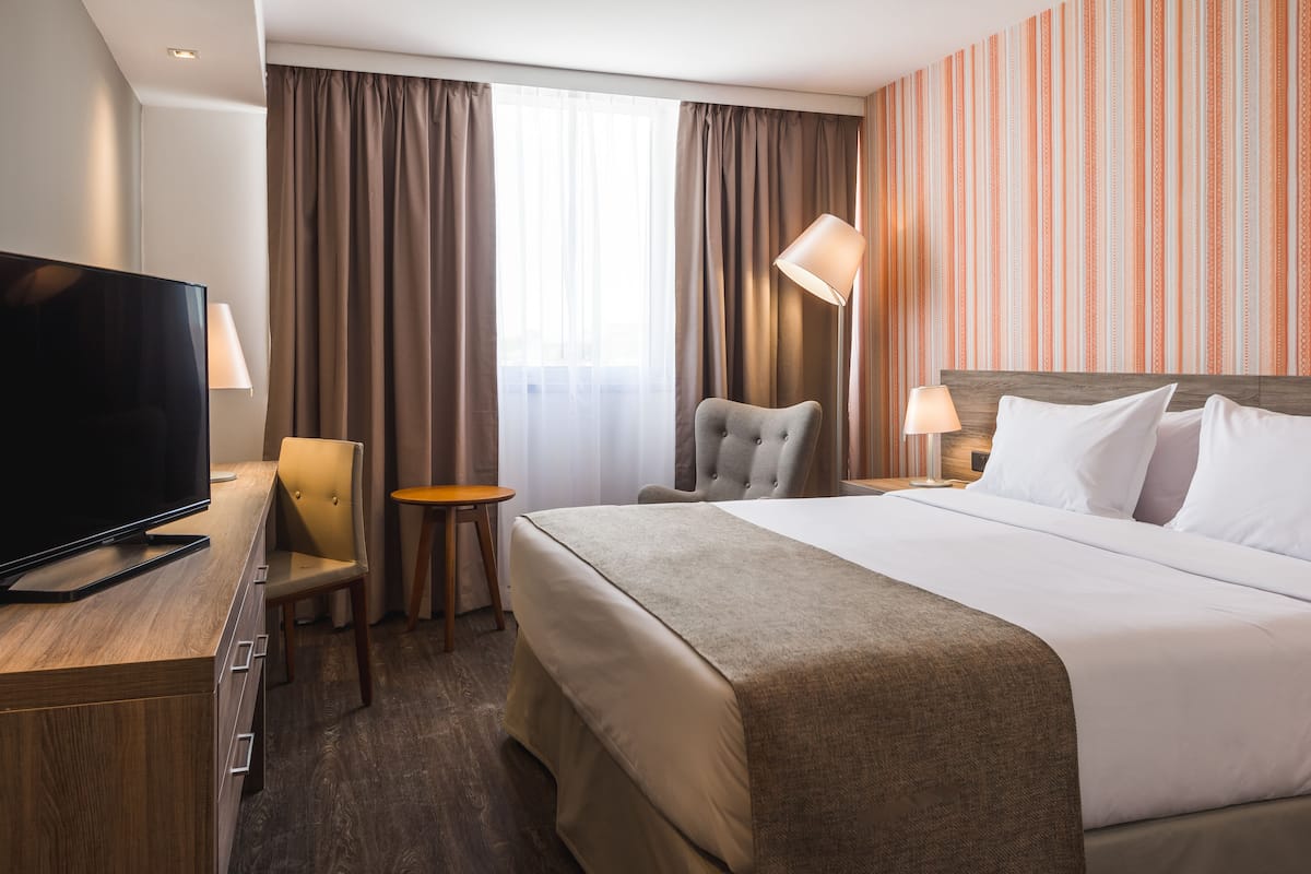 A hotel room with a bed, a TV, a desk, a chair, a lamp, and curtains.