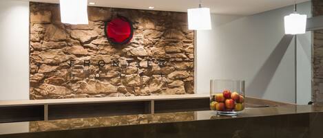 Una zona de recepción con pared de piedra, un florero de vidrio con manzanas e iluminación colgante.