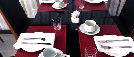 A dining table set with red placemats, white plates, and cutlery.