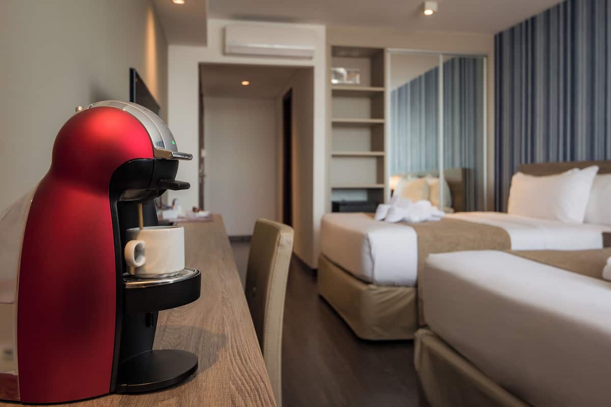A hotel room with a red coffee machine, a bed, a bedside table, and a seating area with a chair.