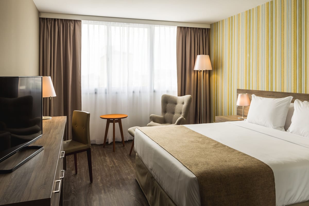 A hotel room with a bed, a TV, a desk, a chair, a small table, and curtains.