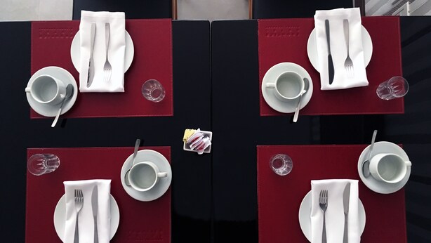 Une table dressée pour quatre personnes, avec de l’argenterie, des couverts et des verres transparents, le tout disposé sur des sets de table rouges.