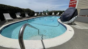 Une piscine avec un escalier en métal, des chaises longues et un barbecue couvert.
