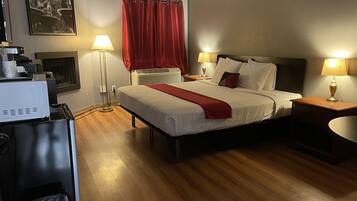 Habitación de hotel con cama, dos mesitas de noche, lámpara, calefactor, un cuadro en la pared y ventana con cortinas rojas.