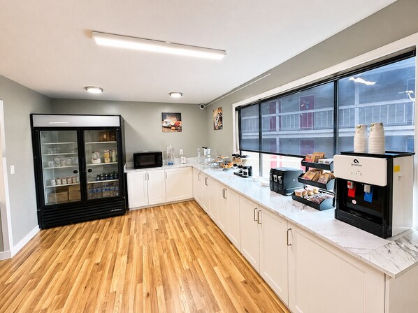 A modern kitchen with a refrigerator, microwave, coffee machine, and a large window.