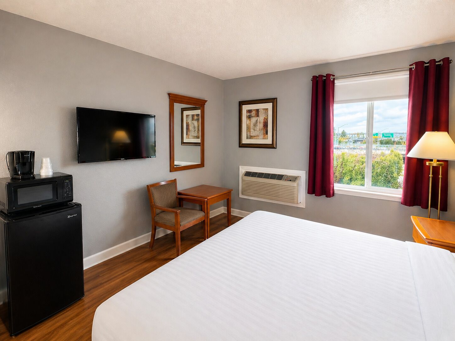 A hotel room with a bed, a desk, a chair, a television, a coffee maker, an air conditioner, and a window with curtains.