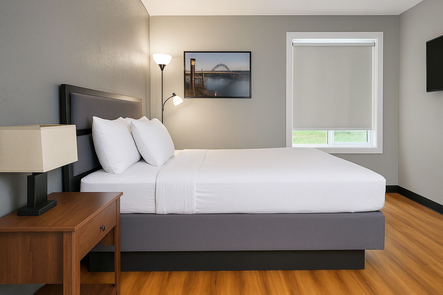 Een moderne slaapkamer met een bed, nachtkastje, lamp en een ingelijste foto aan de muur.