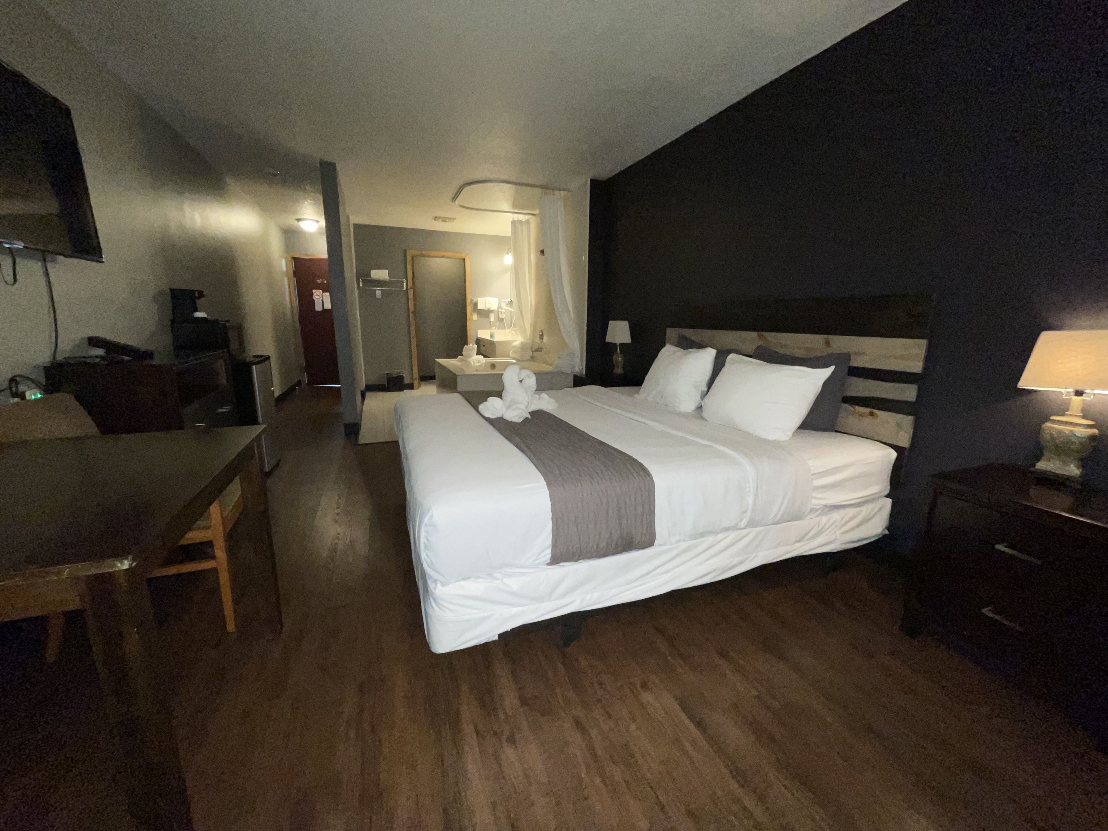 Camera d'albergo con un letto grande, una scrivania, una sedia, una televisione e un bagno visibile attraverso una porta aperta.