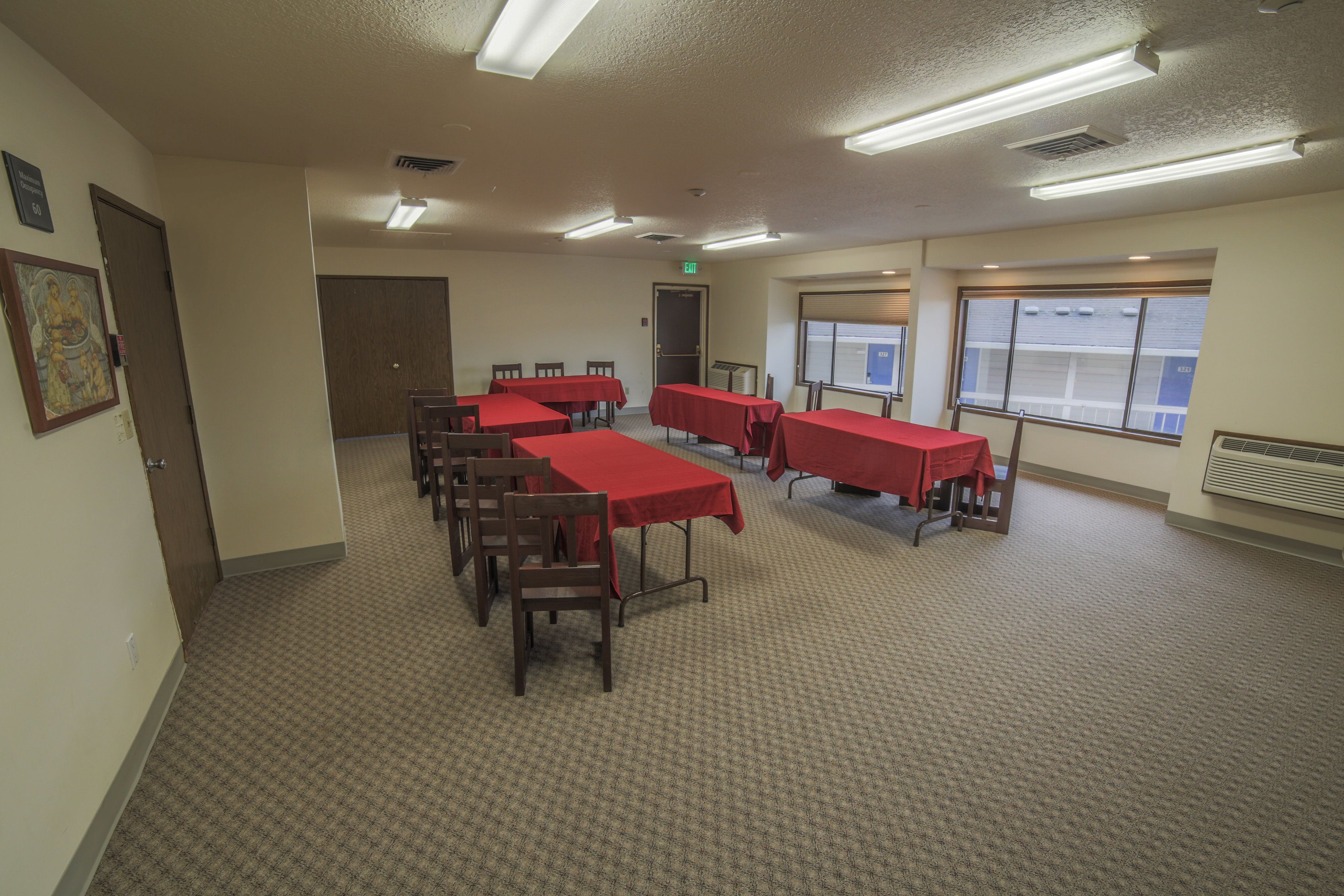 A conference room with multiple tables and chairs, carpeted floor, and large windows with blinds.