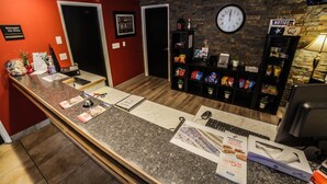 Un comptoir d’accueil avec une horloge, une pancarte indiquant « Responsable de service présent », une pancarte « AVIS » et des étagères remplies de collations.