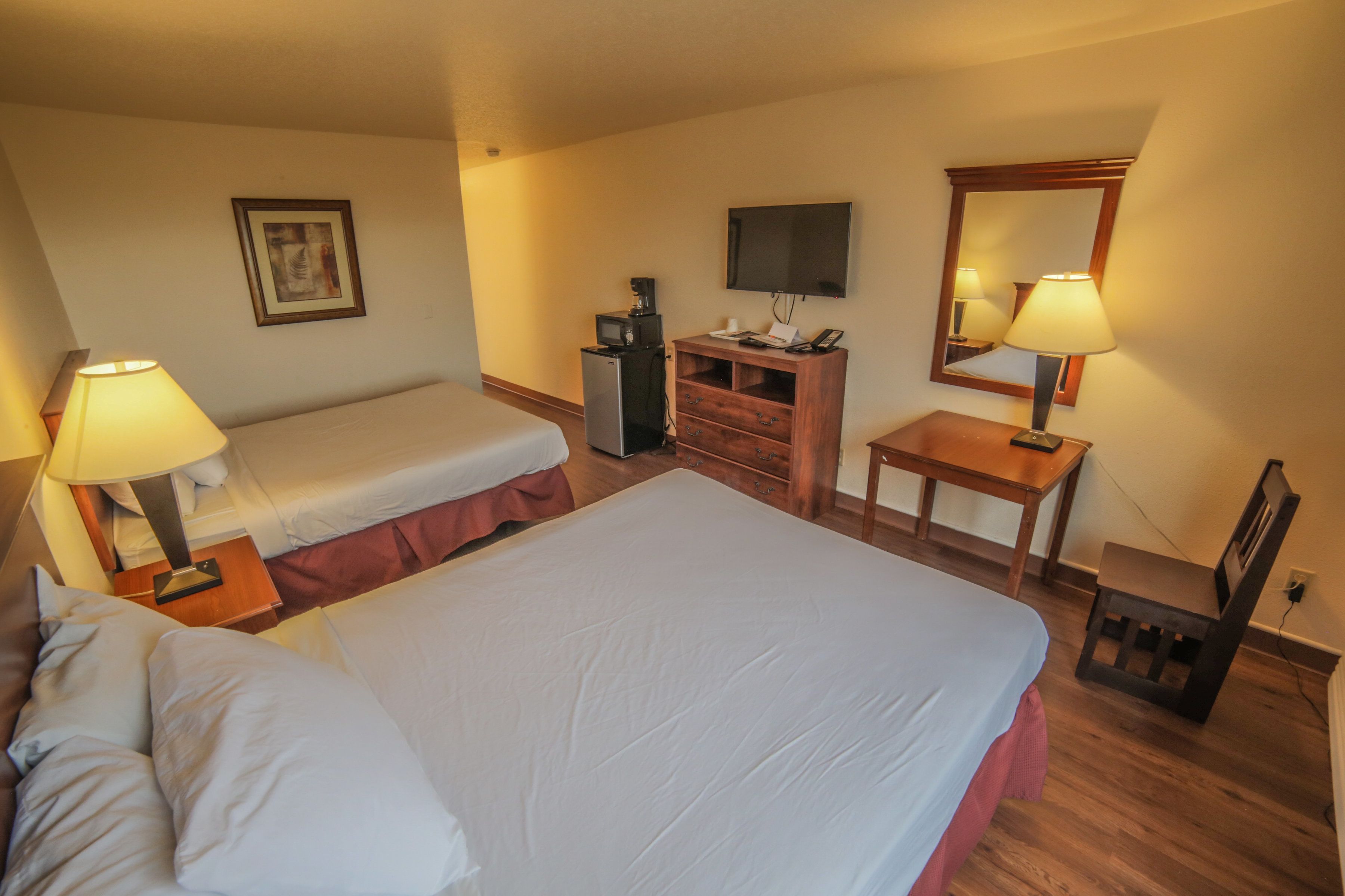 Habitació d'hotel amb un llit gran, un llit més petit, una escriptori, una televisió, un mirall i un aparador.