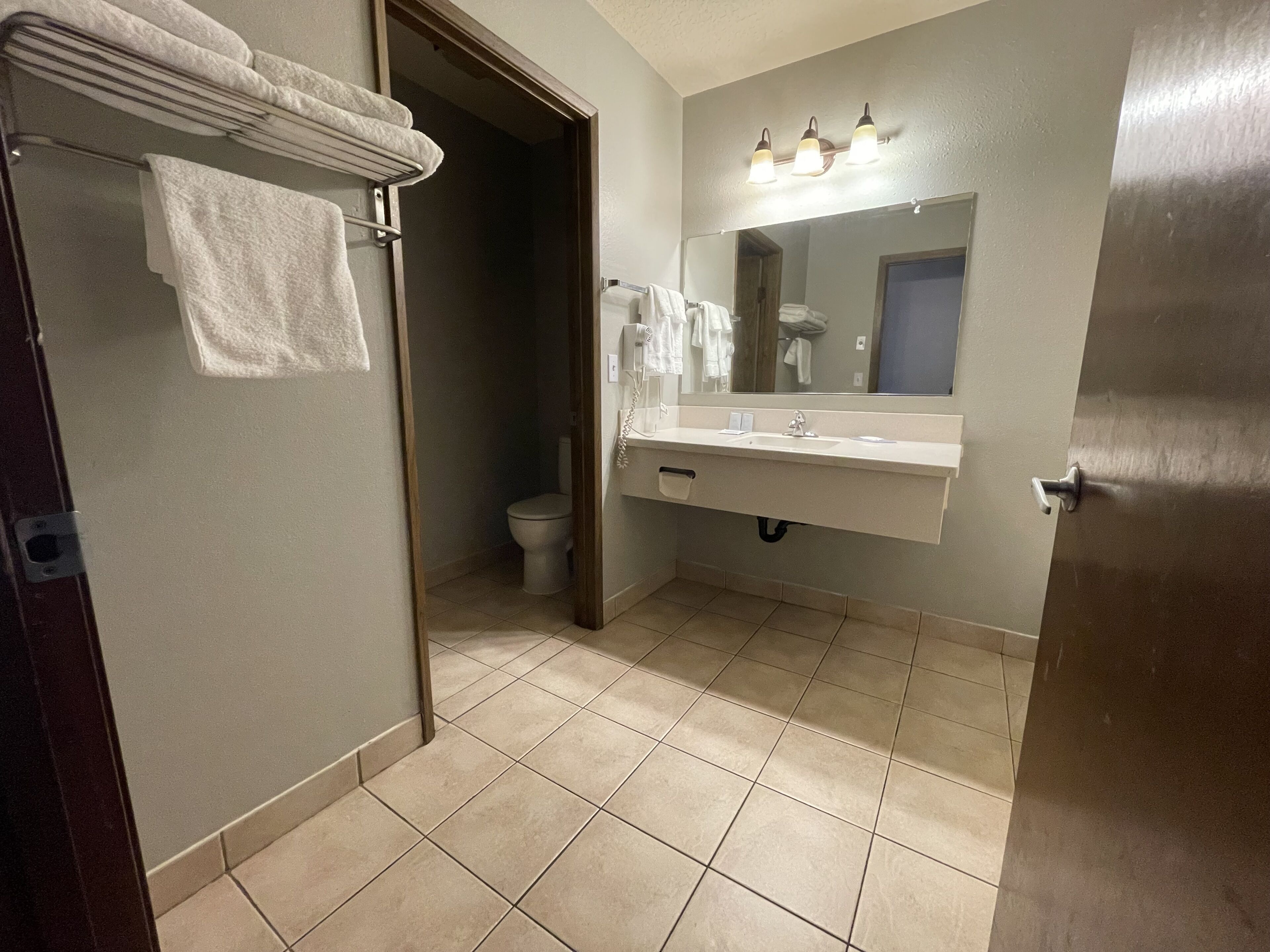 A bathroom with a toilet, sink, and mirror. There are towels hanging on a rack.