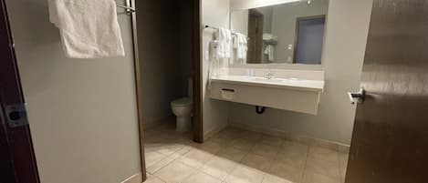A bathroom with a toilet, sink, and mirror. There are towels hanging on a rack.