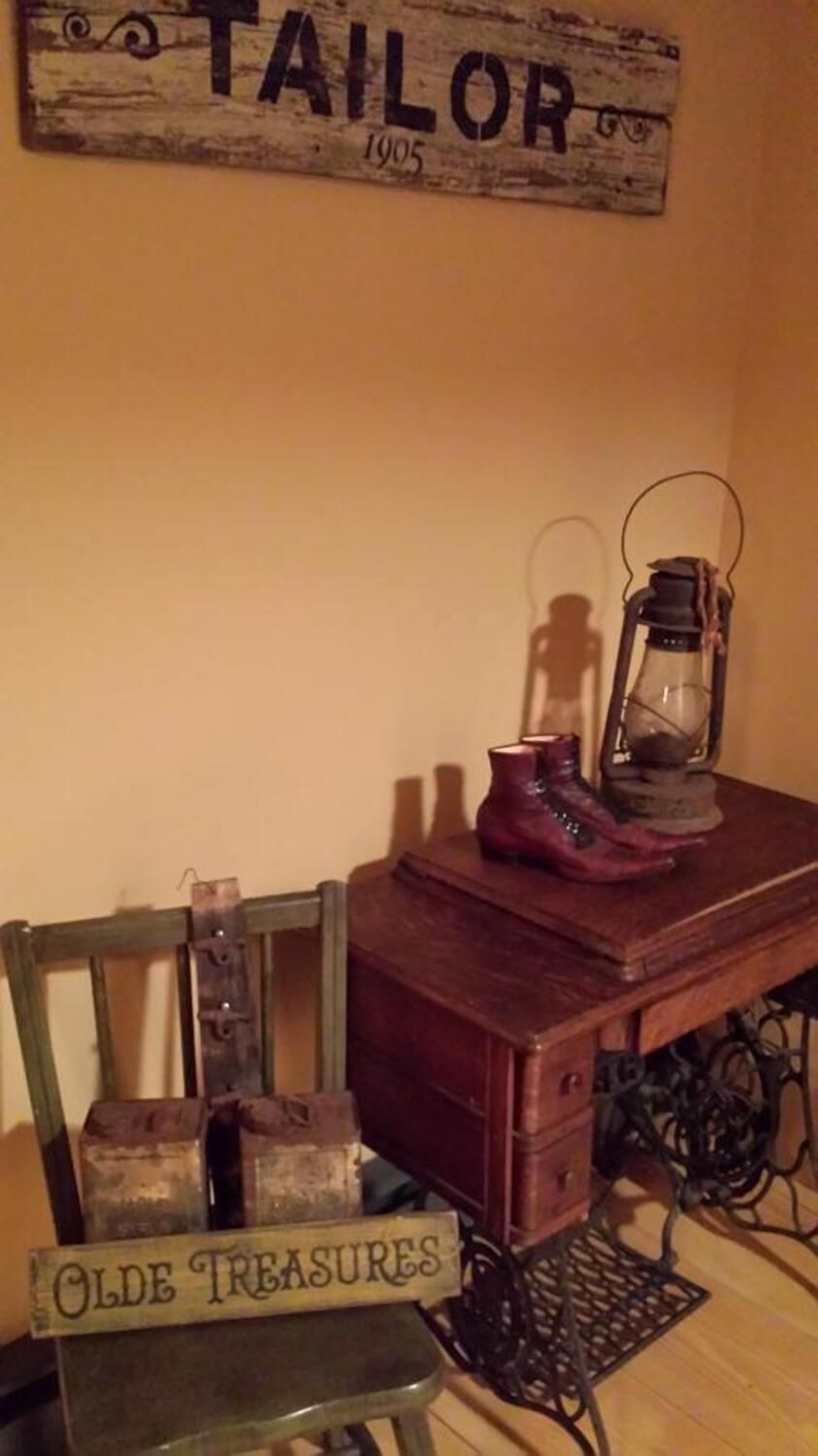 A vintage-themed display with a wooden sign reading "TAILOR 1905," a pair of boots, a lantern, and a chair labeled "OLDE TREASURES."
