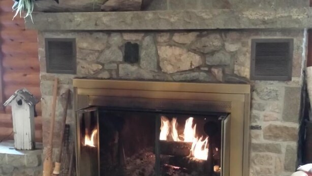 A stone fireplace with a fire burning inside, a cat on the mantel, and a rustic wooden interior.