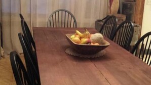 A dining room with a wooden table, chairs, and a fruit bowl.