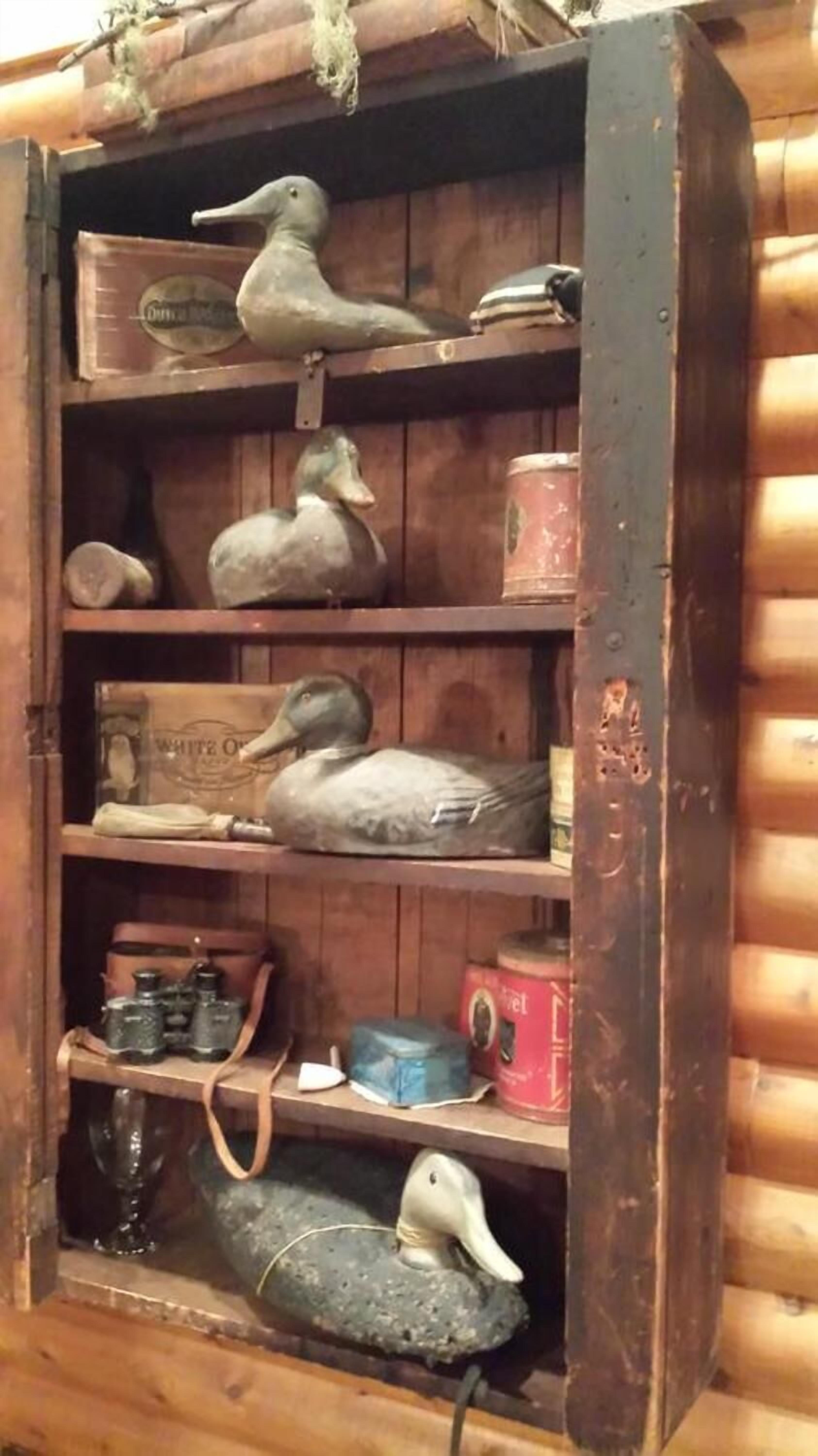 A wooden shelf with various items including duck figurines, binoculars, and boxes.