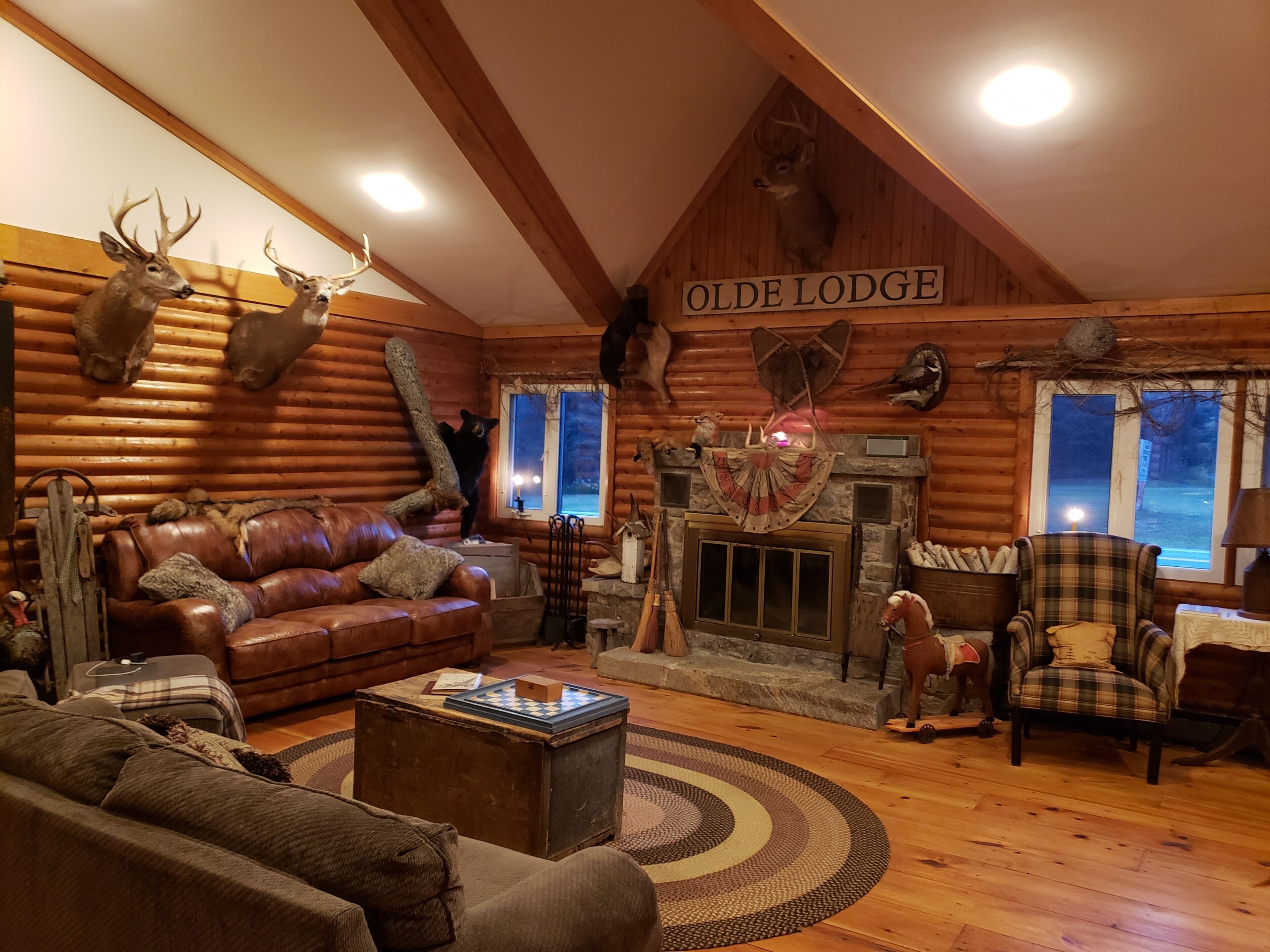 A log cabin interior with a fireplace, leather furniture, and mounted animal heads.