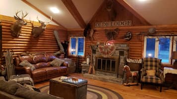 A log cabin interior with a fireplace, leather furniture, and mounted animal heads.