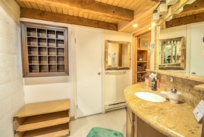A bathroom with a wooden ceiling, a window with a grid pattern, a white sink, and a mirror with a wooden frame. - Ski Time Square by Retreatia (Steamboat Springs)