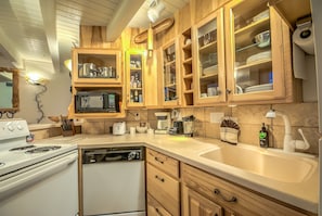 A kitchen with wooden cabinets, a white stove, a dishwasher, and a sink. - Ski Time Square by Retreatia (Steamboat Springs)