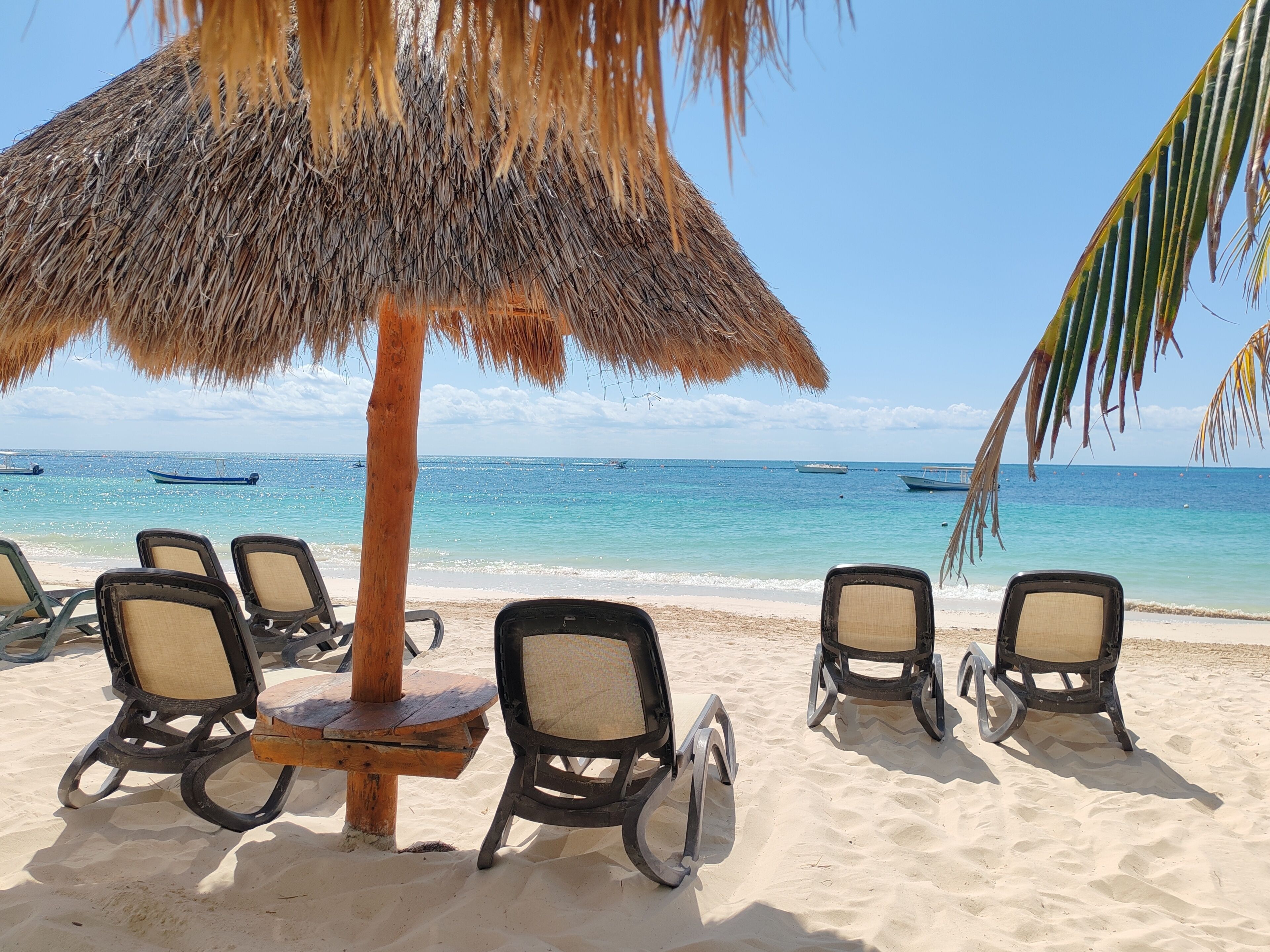 A beach with thatched umbrellas, lounge chairs, and a view of the ocean with boats.