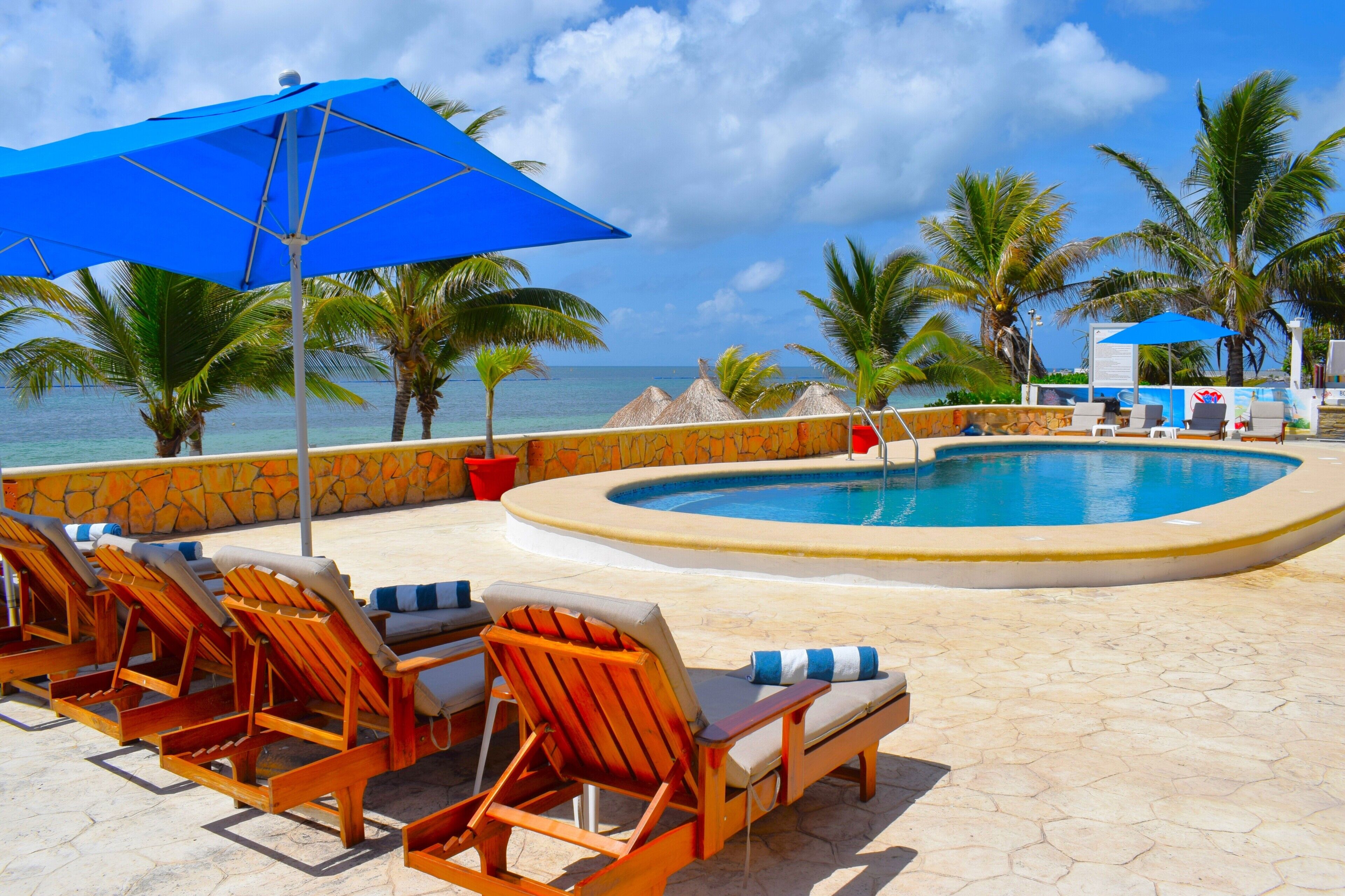 A poolside area with lounge chairs, a blue umbrella, and a view of the ocean.
