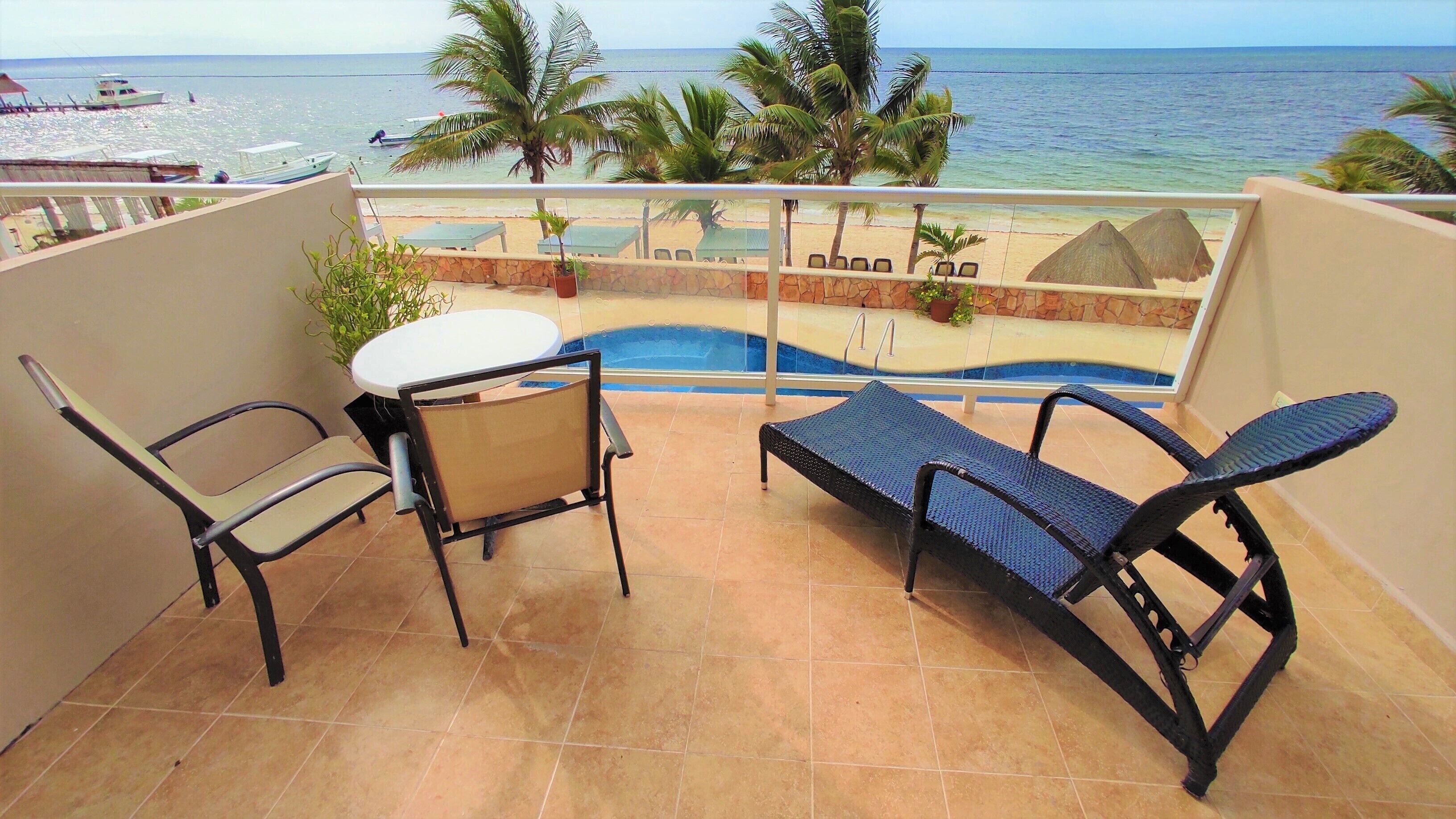 A balcony with a table and chairs, a small pool, and a view of the beach and ocean.