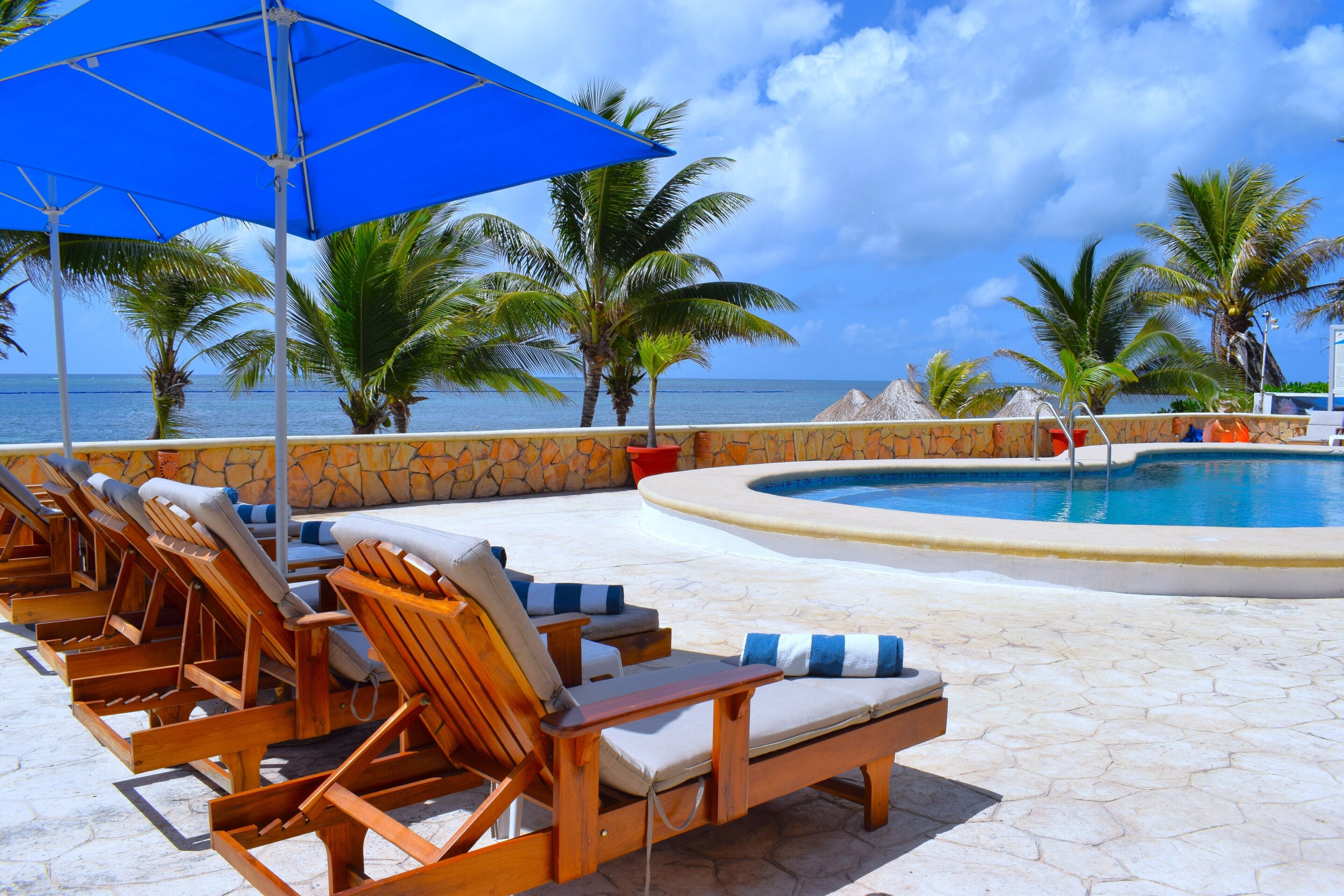 Un espace aménagé au bord de la piscine, avec des chaises longues, un parasol bleu et une vue sur l’océan.