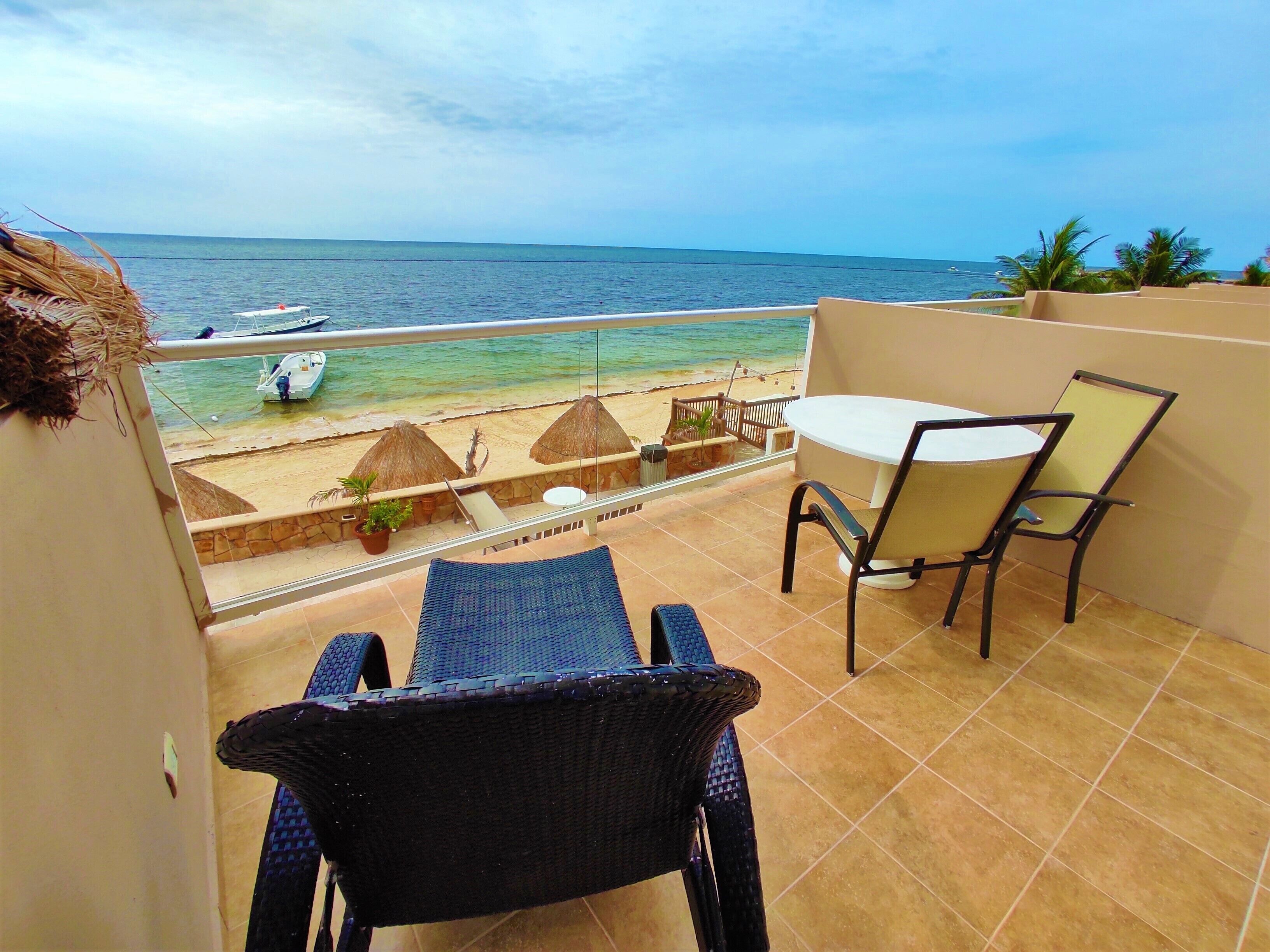 Uma varanda com vista para o oceano, uma mesa com cadeiras e um pequeno jardim com plantas em vasos.