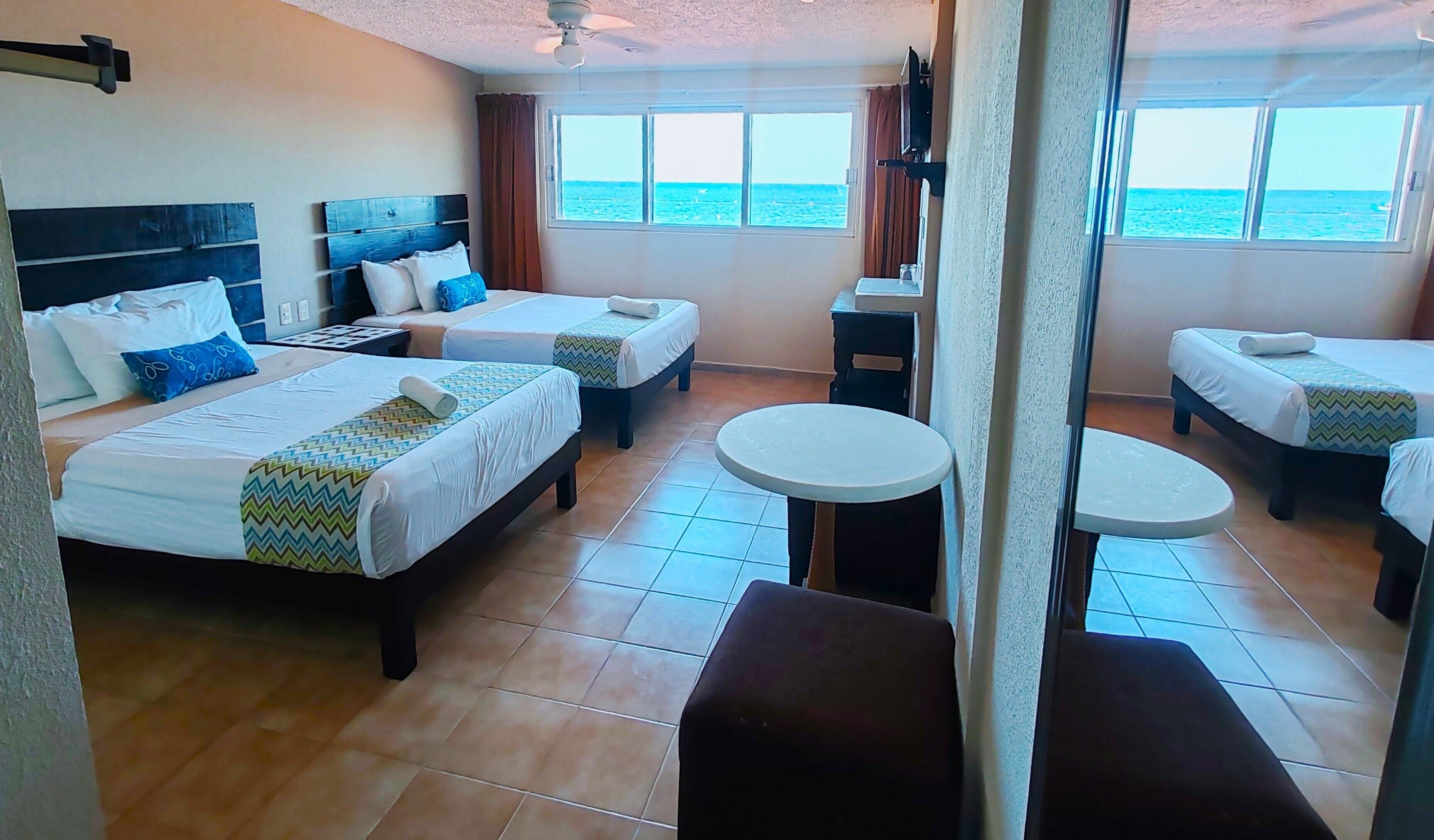 A hotel room with two beds, a small round table, and a view of the sea.