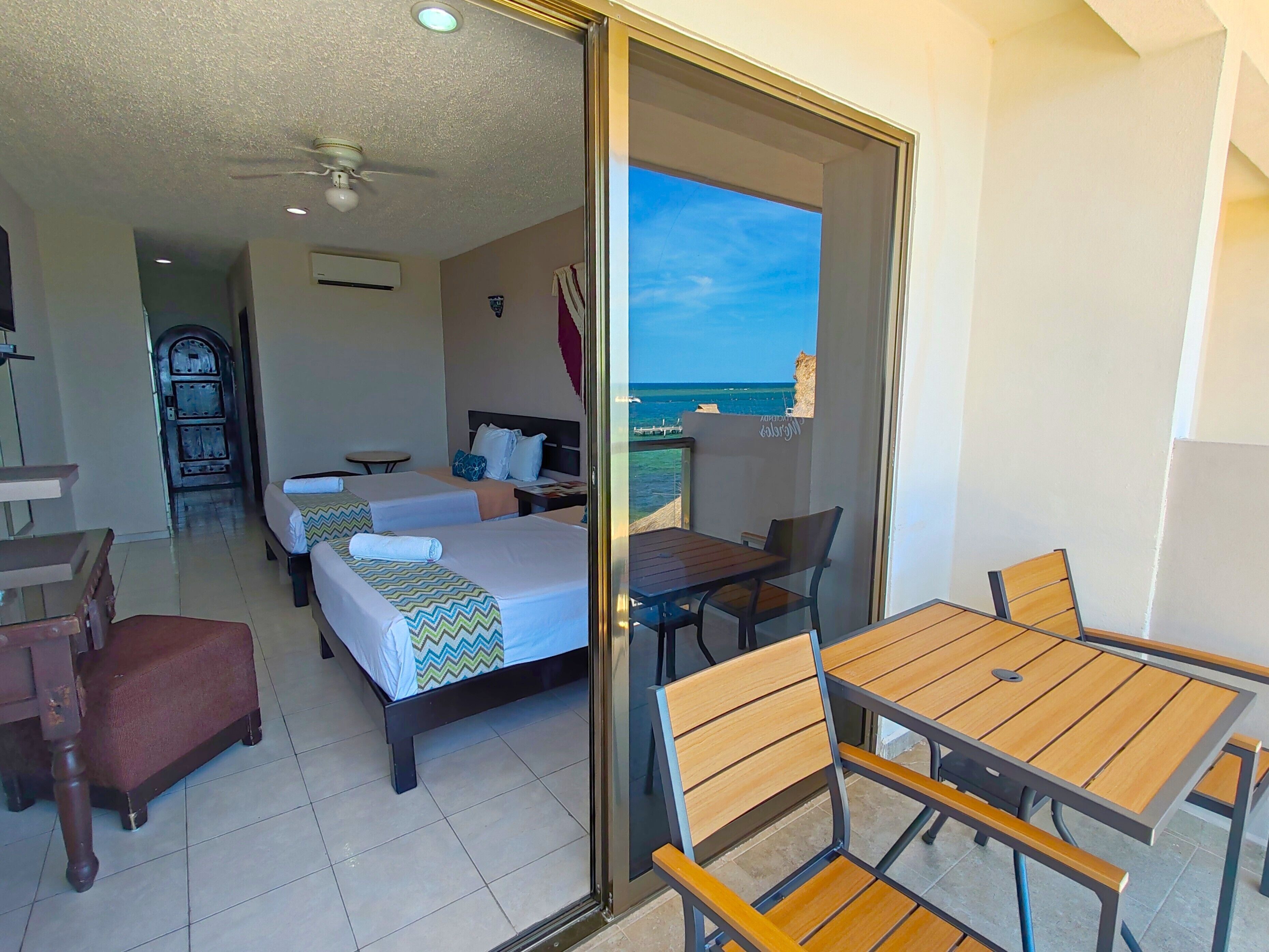 A hotel room with two beds, a balcony with a table and chairs, and a view of the sea.