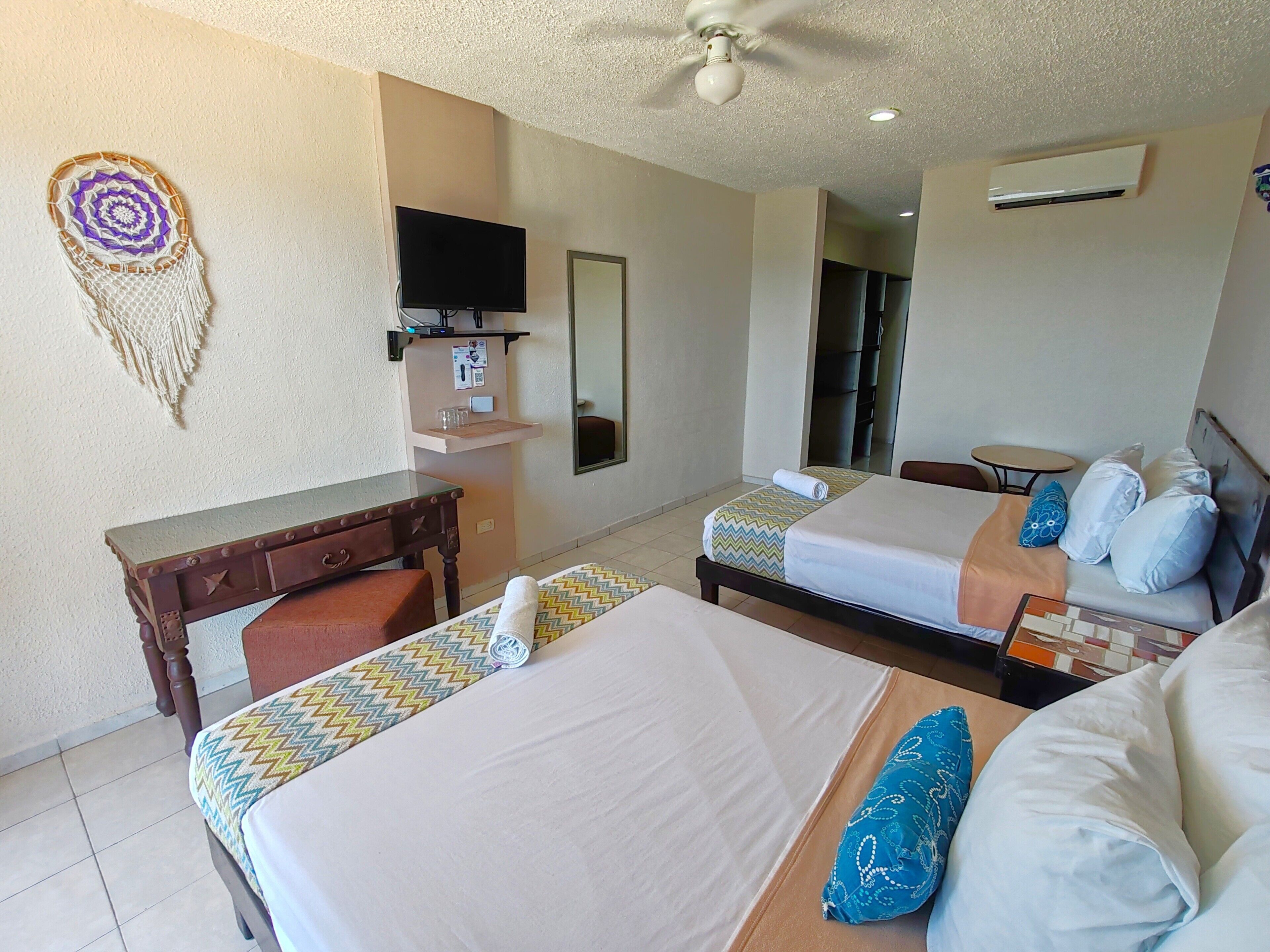 A hotel room with two beds, a desk, a television, and a ceiling fan.