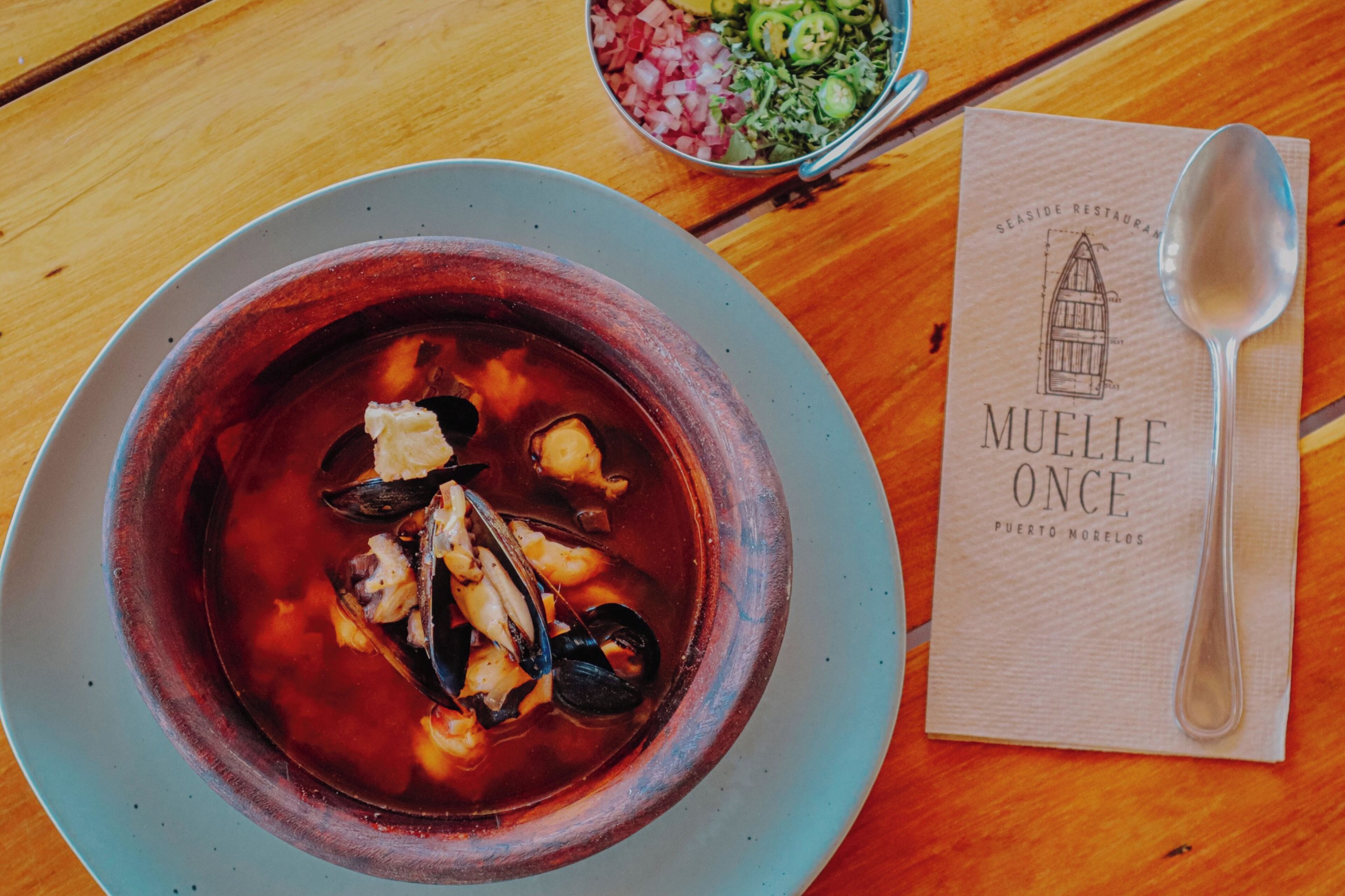 Uma tigela de sopa de marisco sobre uma mesa, com uma colher e um menu.
