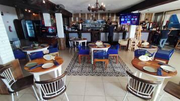 A restaurant with multiple tables and chairs, a bar area with a TV screen, and a patterned floor.