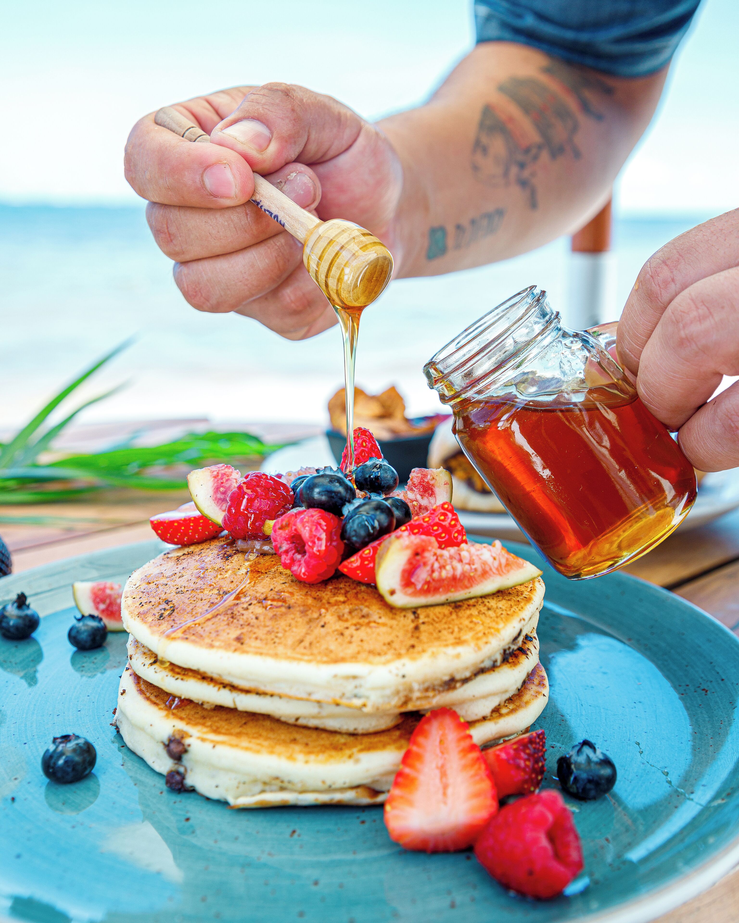 Una pila di pancake con frutti di bosco freschi e miele che viene versato sopra.