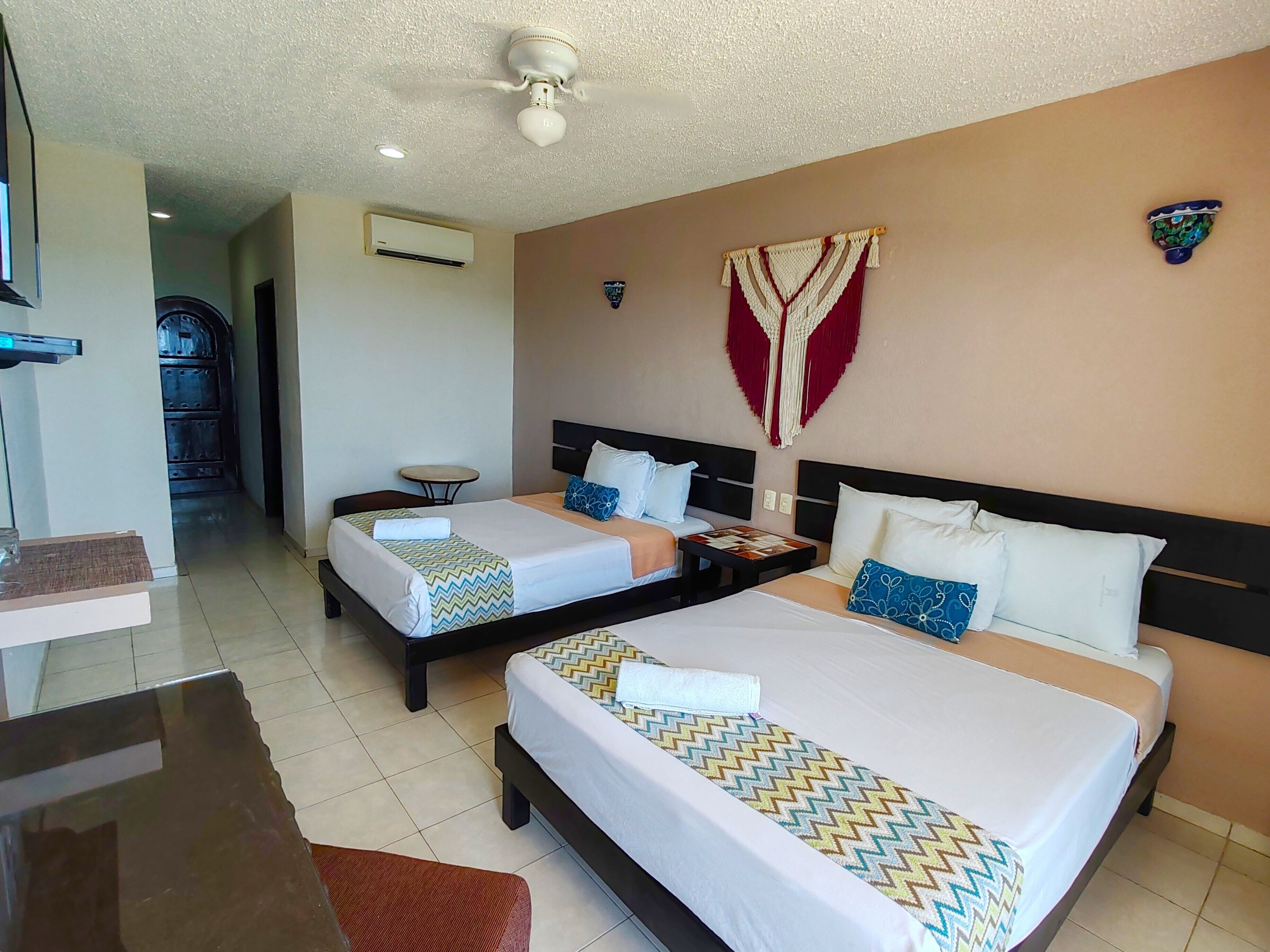 Habitación de hotel con dos camas, una mesita pequeña, una silla, unidad de aire acondicionado y ventilador de techo.