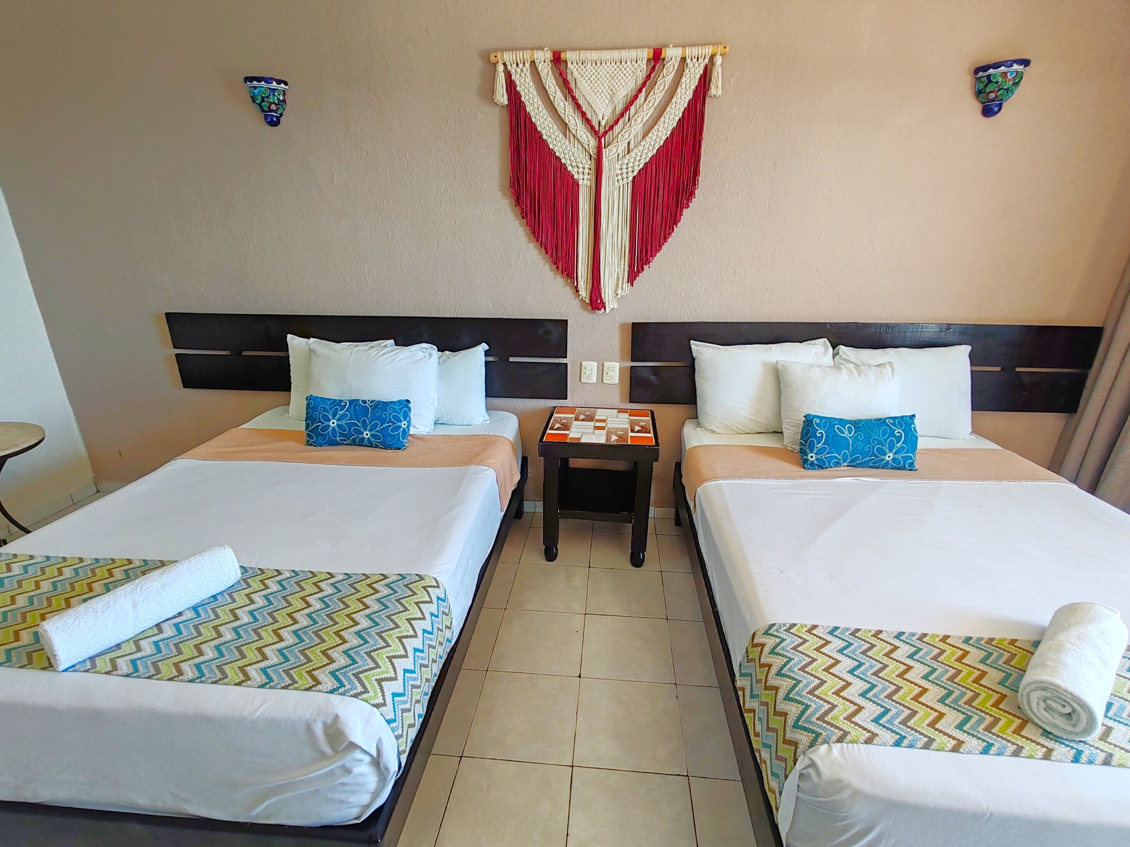 A hotel room with two beds, a small table, and a wall hanging.