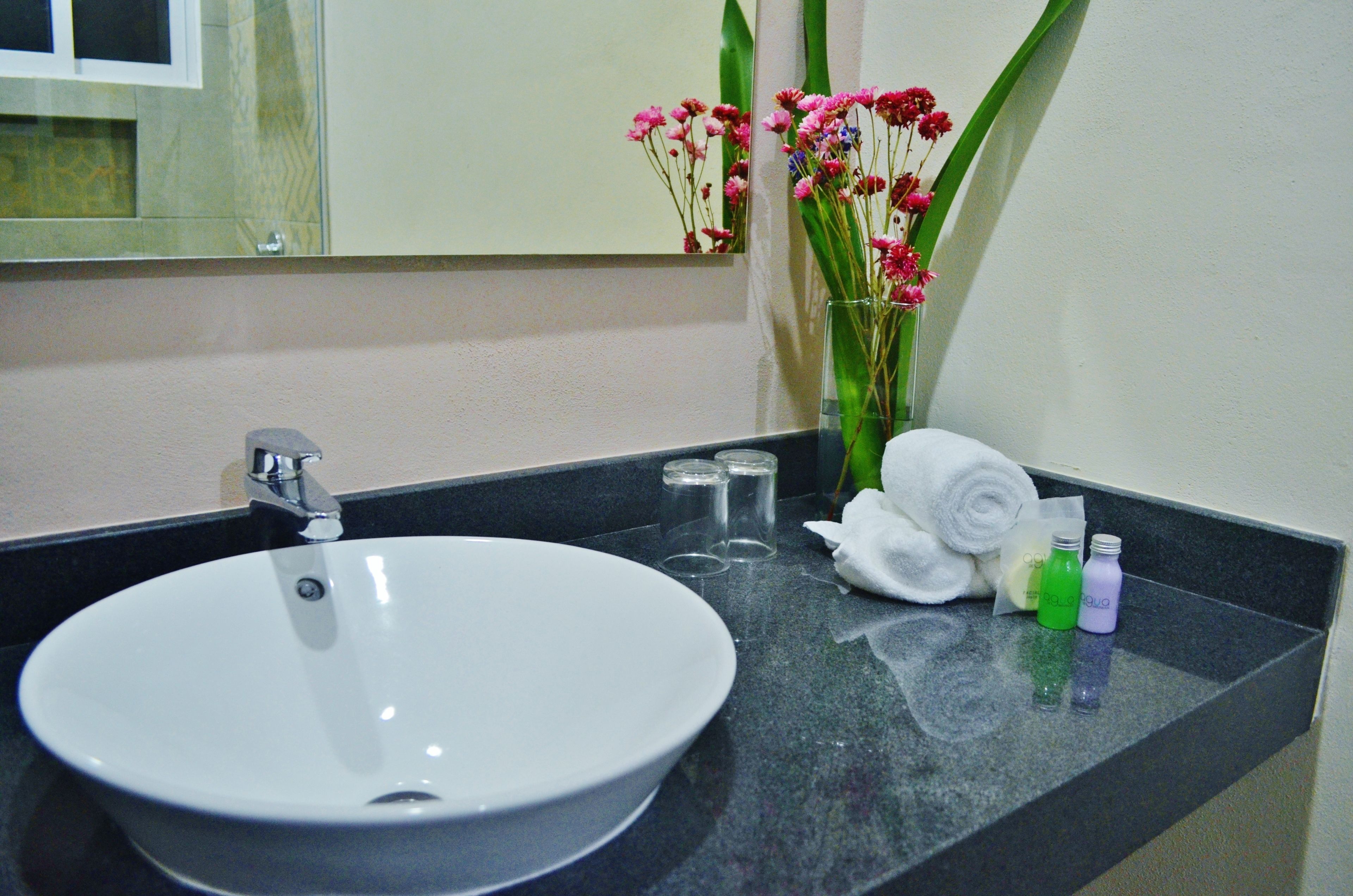 A bathroom sink with a mirror, a vase with flowers, and toiletries on the countertop.