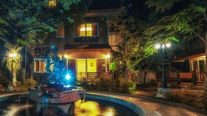 A nighttime view of a hotel with a central fountain, surrounded by trees and illuminated by street lamps. - Khaoyai Kirithantip Resort (Pak Chong)