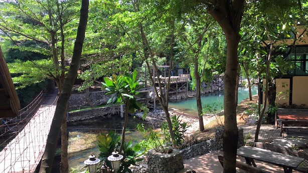 A serene outdoor area with a wooden bridge, stone structures, and a tranquil water body surrounded by lush greenery. - Khaoyai Kirithantip Resort (Pak Chong)