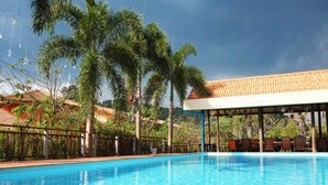 A clear blue swimming pool with a covered seating area and palm trees in the background. - Khaoyai Kirithantip Resort (Pak Chong)