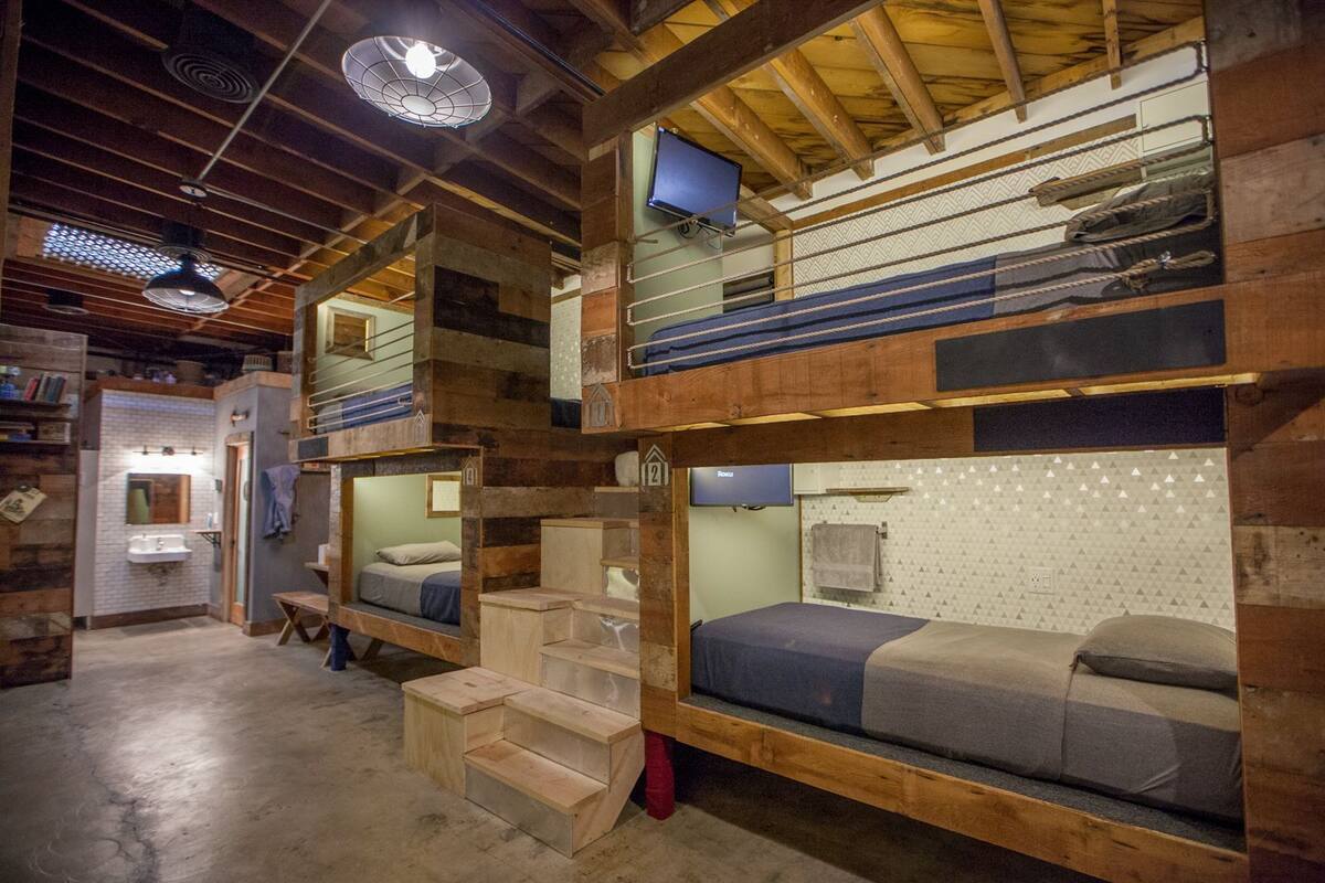 A multi-level bunk bed room with a television on the upper bunk, a small bathroom with a sink, and a staircase leading to the upper bunk.