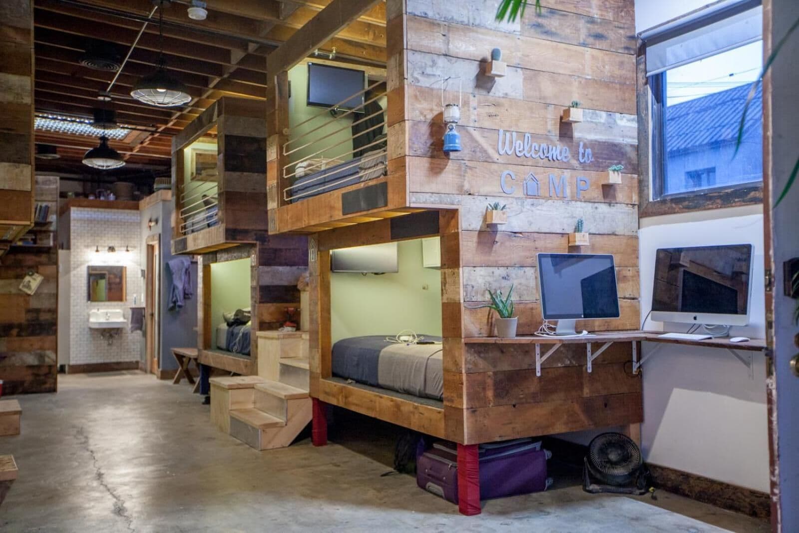A rustic cabin-style room with bunk beds, a work desk with a computer, and a welcome sign.