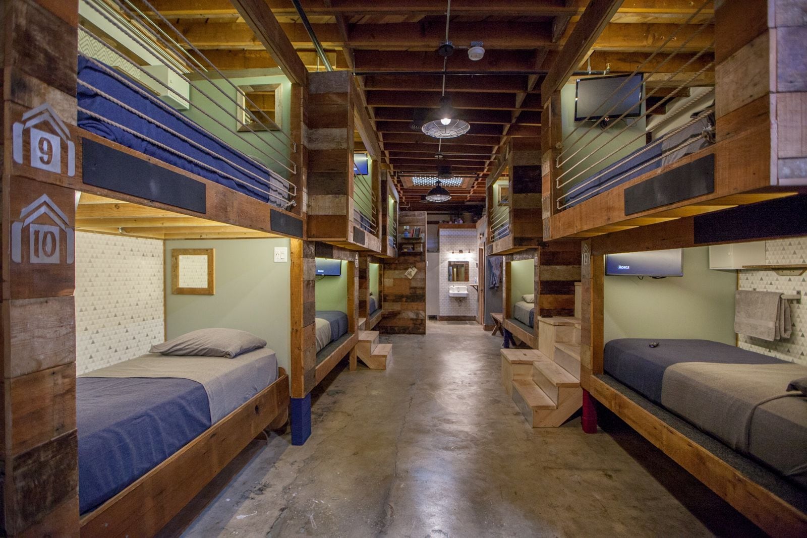 A dormitory-style room with bunk beds, wooden walls, and a central hallway.