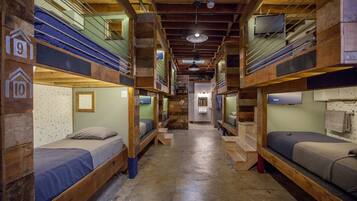 A dormitory-style room with bunk beds, wooden walls, and a central hallway.