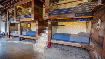 A rustic cabin-style hotel with bunk beds labeled "Brittany" and "Familia," wooden beams, and a concrete floor.